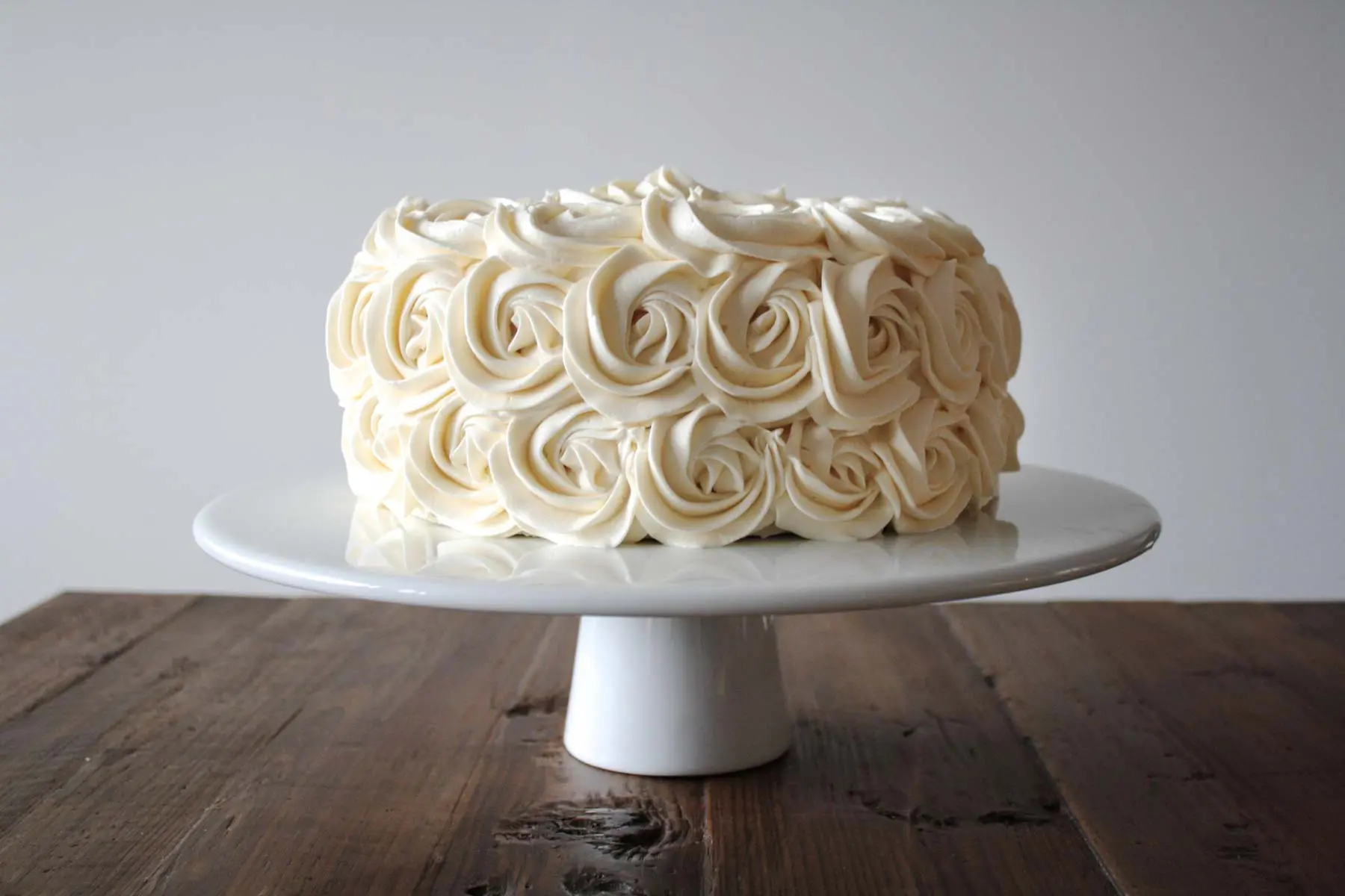 Cake decorated with buttercream rosettes on a white cake stand.