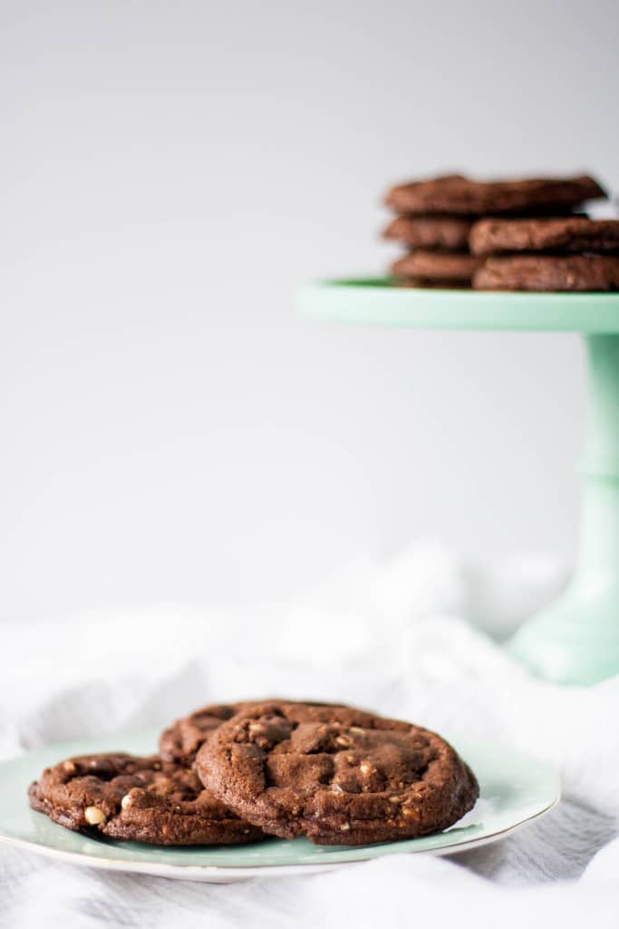 Cookies on a plate with cookies on a cake stand in the background.