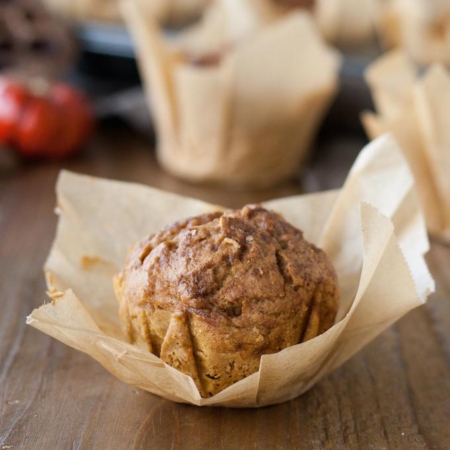Close up of a pumpkin muffin with the parchment liner peeled back.