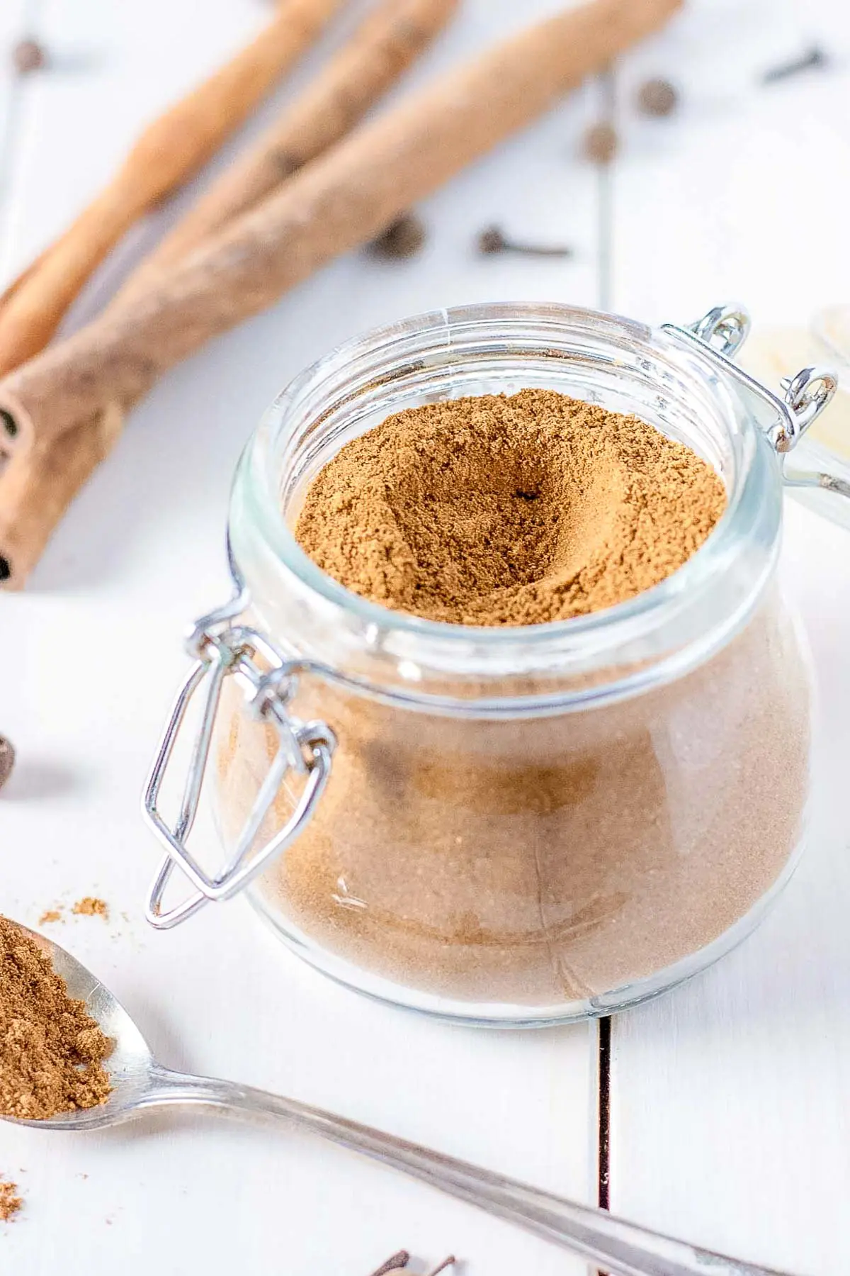 A jar of gingerbread spice with cinnamon sticks behind it.
