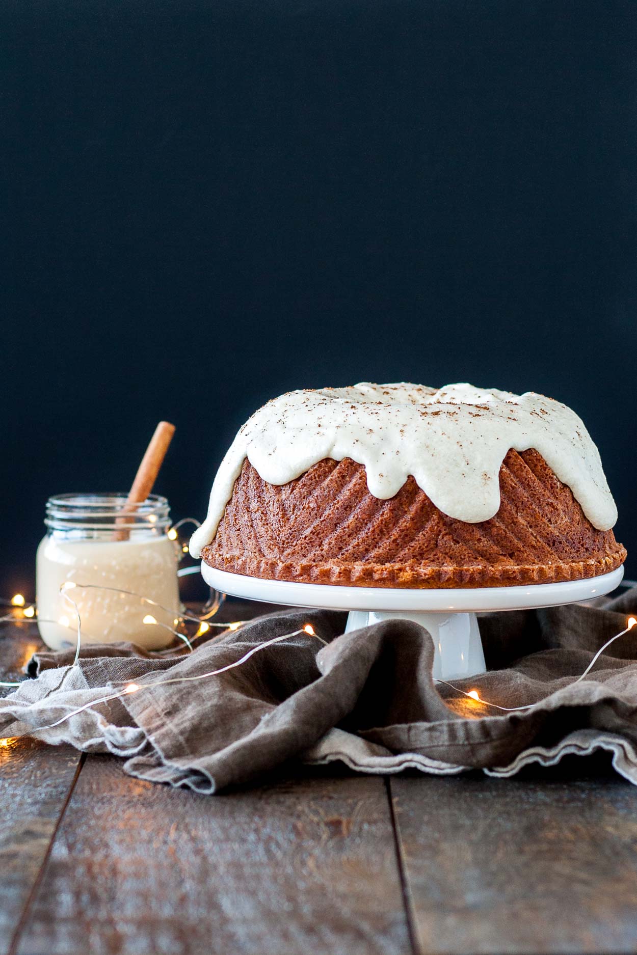 A bundt cake on a white cake stand sitting on top of a wooden table.