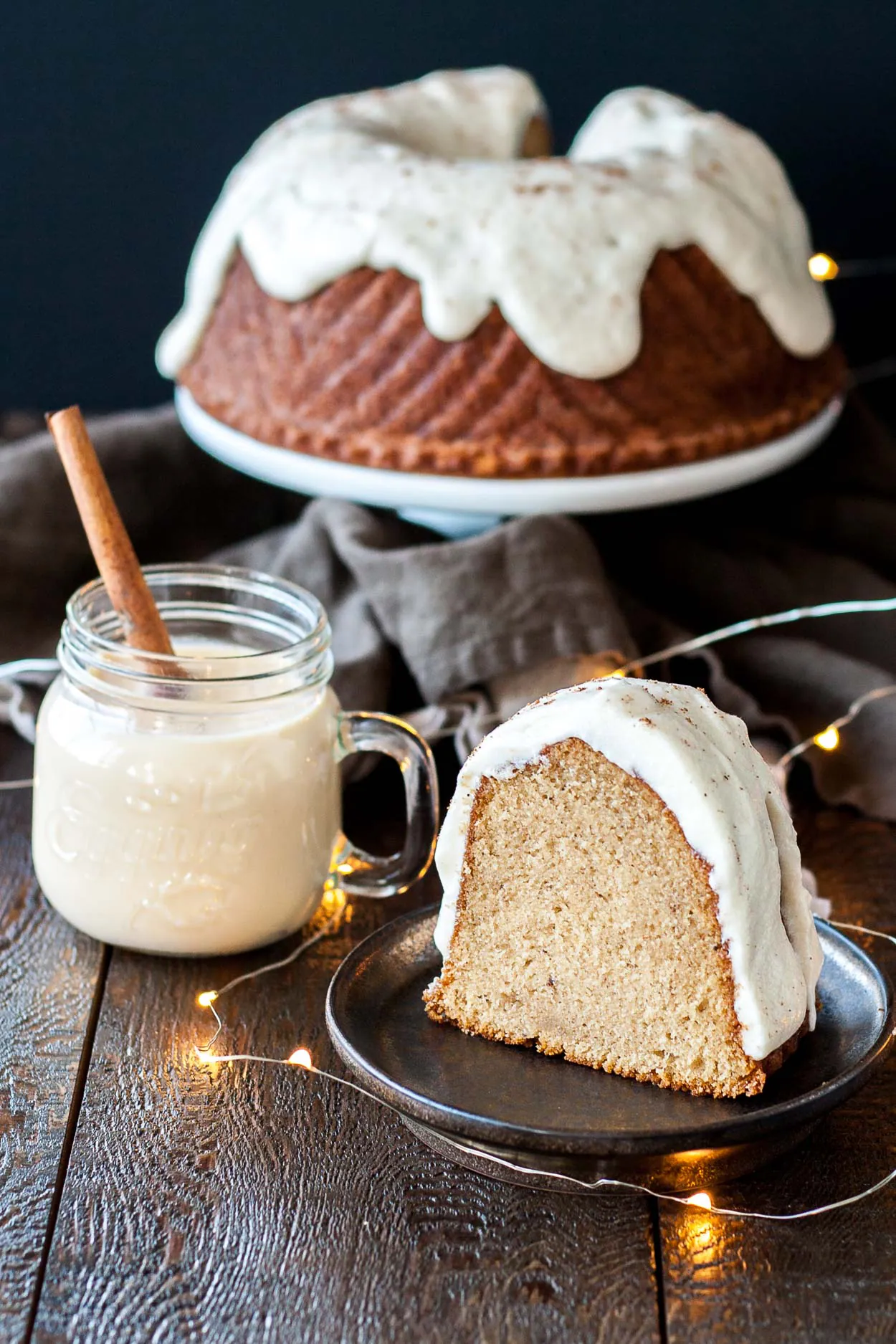 A piece of cake on a plate next to a cup of eggnog