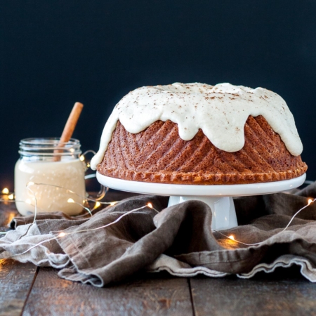 A bundt cake on a white cake stand sitting on top of a wooden table.