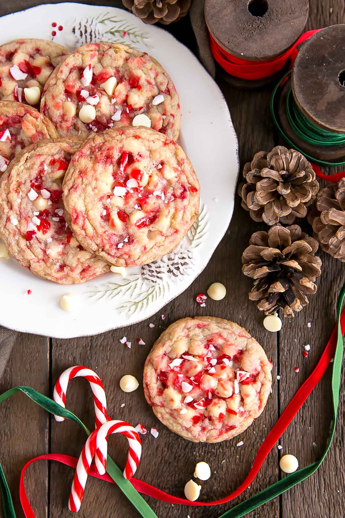 Overhead shot of White Chocolate Candy Cane Cookies on a plate with ribbons and pine cones