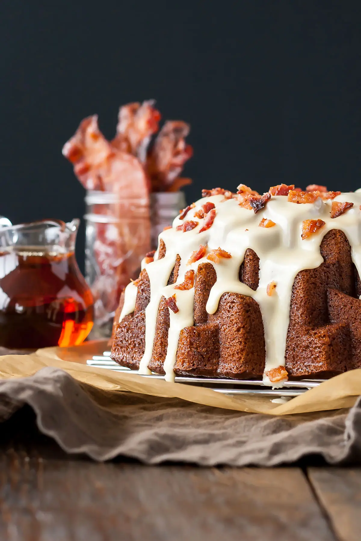 Bundt cake with maple syrup and bacon in the background.