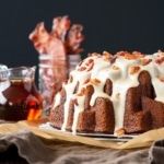 Bundt cake with maple syrup and bacon in the background.
