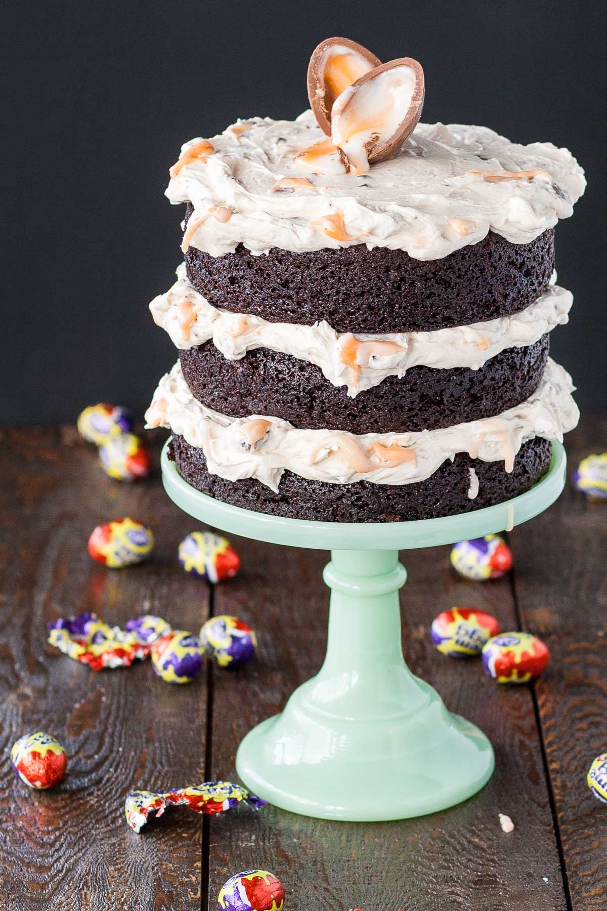 A cake sitting on top of a mint green cake stand. Creme eggs scattered all around.