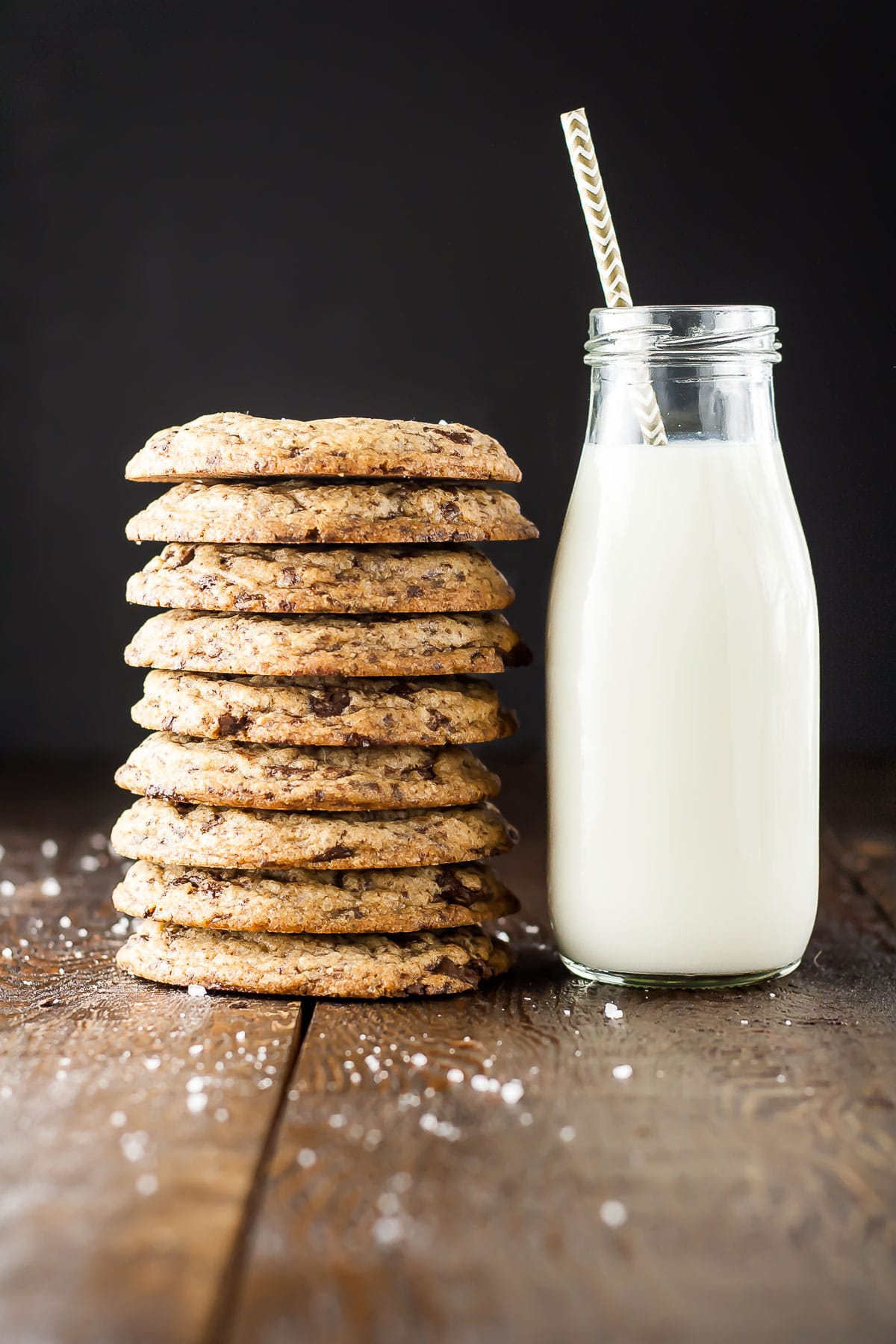 A stack of cookies on a wooden table with a small pitcher of milk beside it.