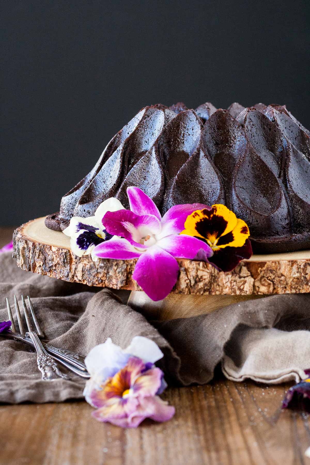 Chocolate Bundt cake on a wooden cake stand garnished with fresh edible flowers.