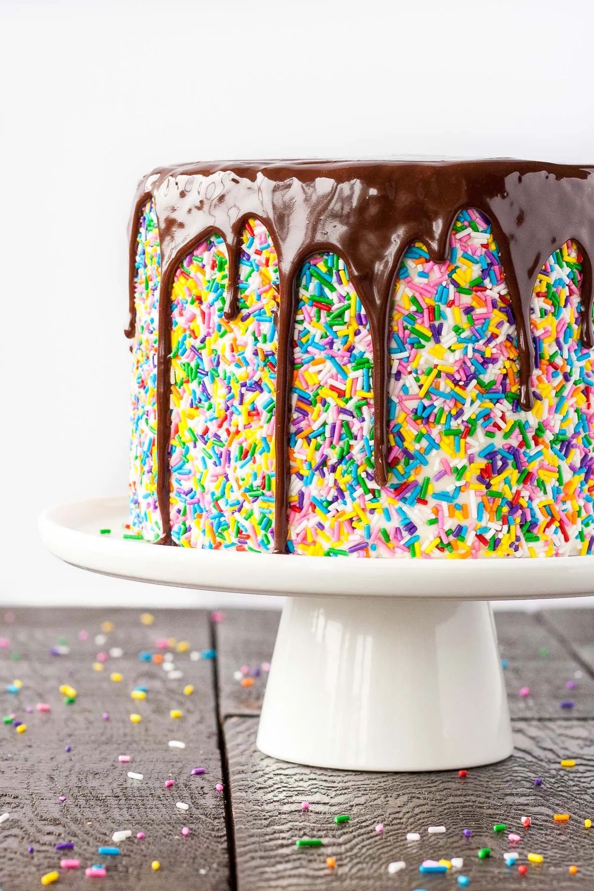 Funfetti cake with a chocolate ganache drip on a white cake stand.