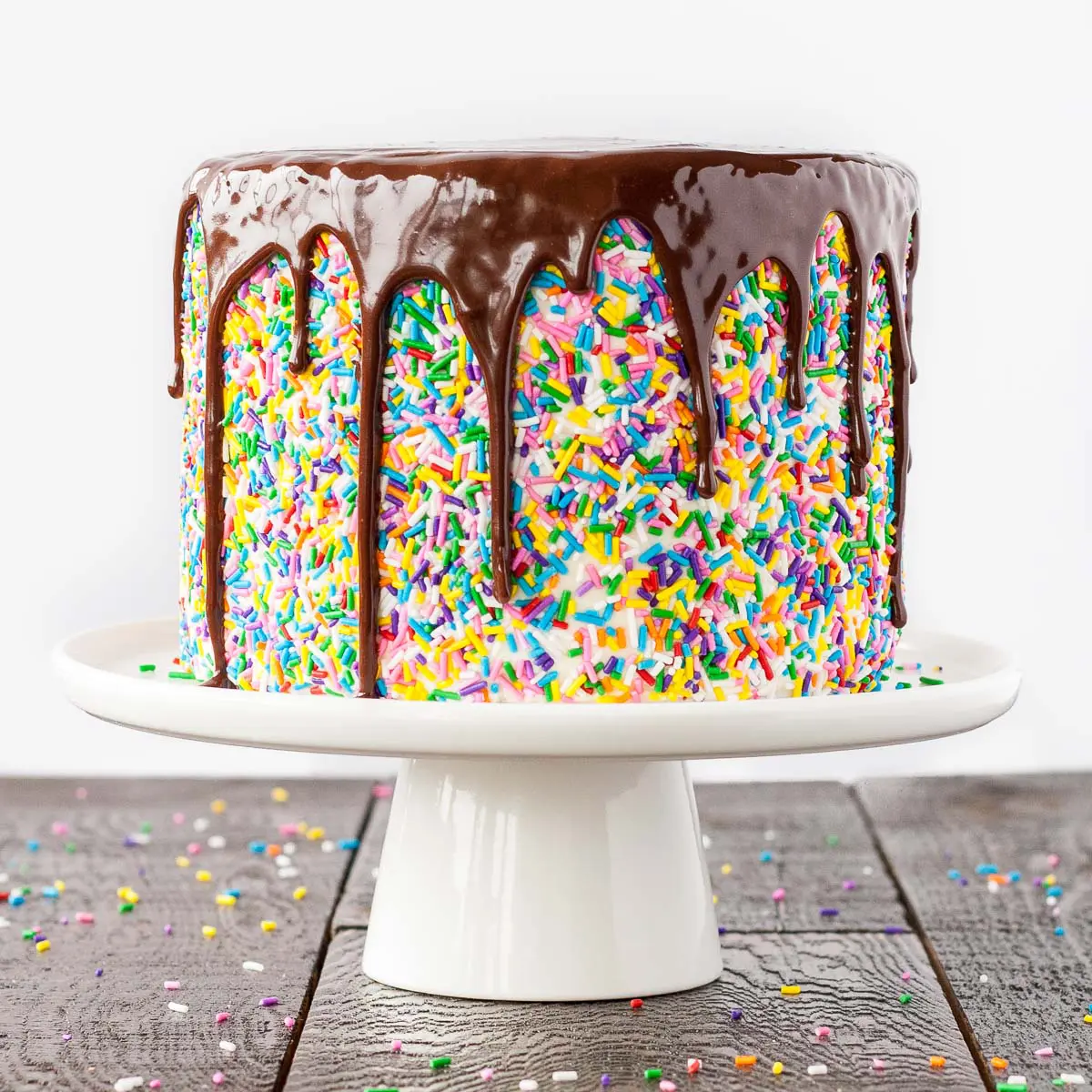 Funfetti cake with a chocolate ganache drip on a white cake stand. 