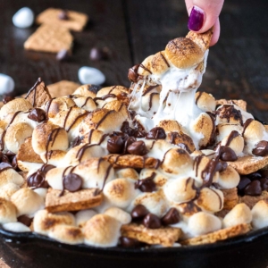 S'mores nachos in a cast iron skillet. Fingers pulling out one of the 