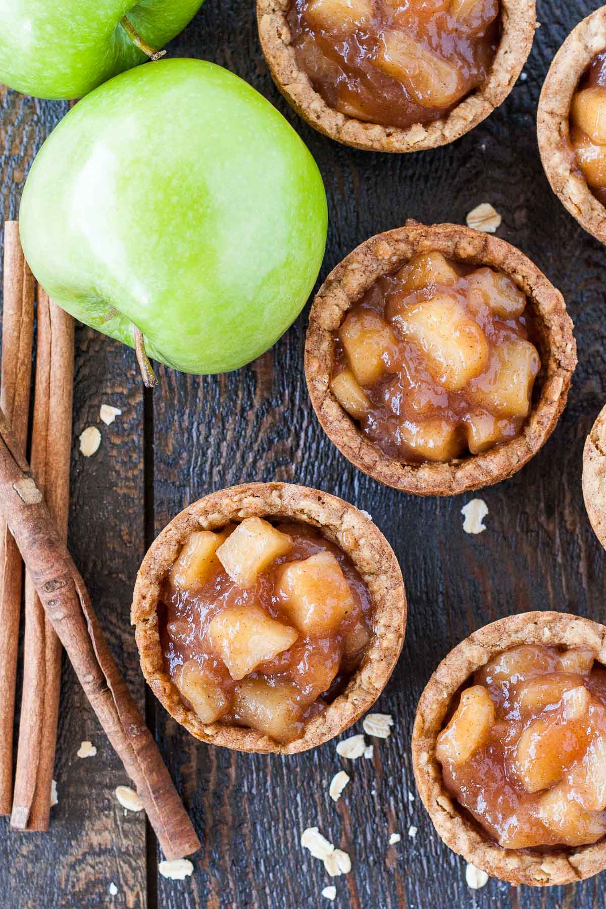 Overhead photo of apple crisp cookie cups with apples and cinnamon sticks on the side.