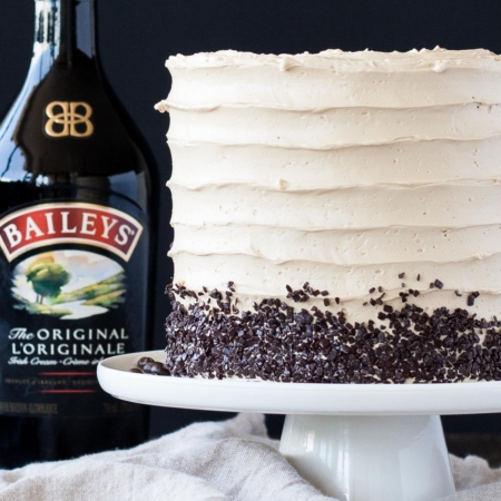 Cake on a white cake stand with a bottle on Baileys behind it.