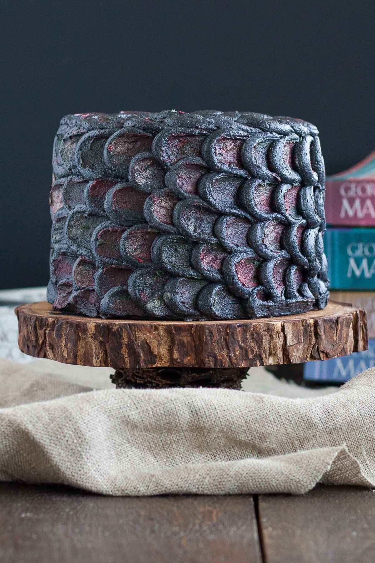 Cake decorated with dragonscales on a rustic cake stand with Game of Thrones books in the background.