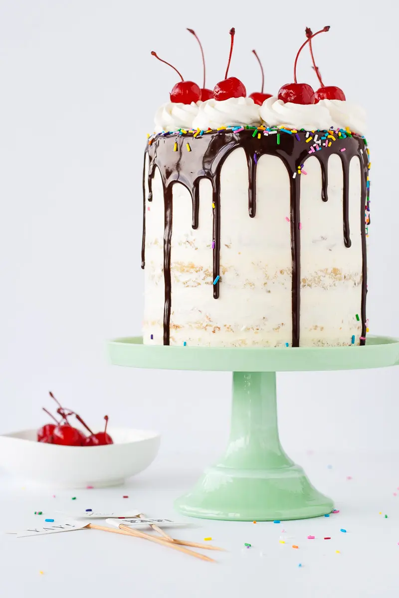 A cake sitting on top of a mint green cake stand with a small bowl of cherries beside it.