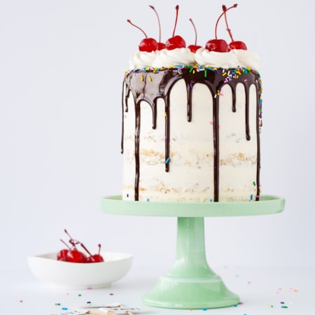 A cake sitting on top of a mint green cake stand with a small bowl of cherries beside it.