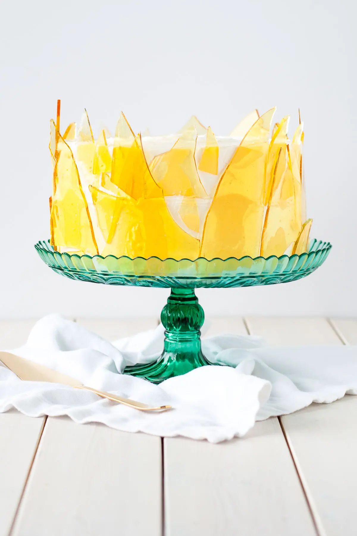 Cake with candied sugar shards on the side of it on a green cake stand.