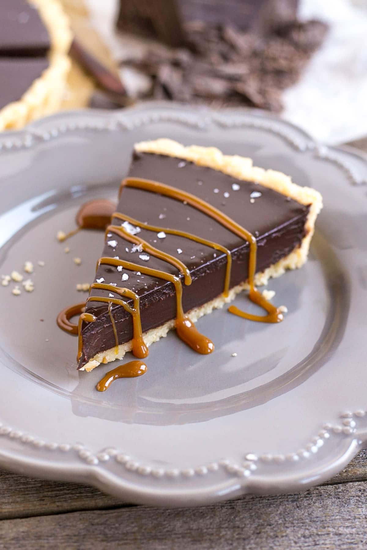 Close up of a slice of chocolate ganache tart on a plate with caramel drizzle.