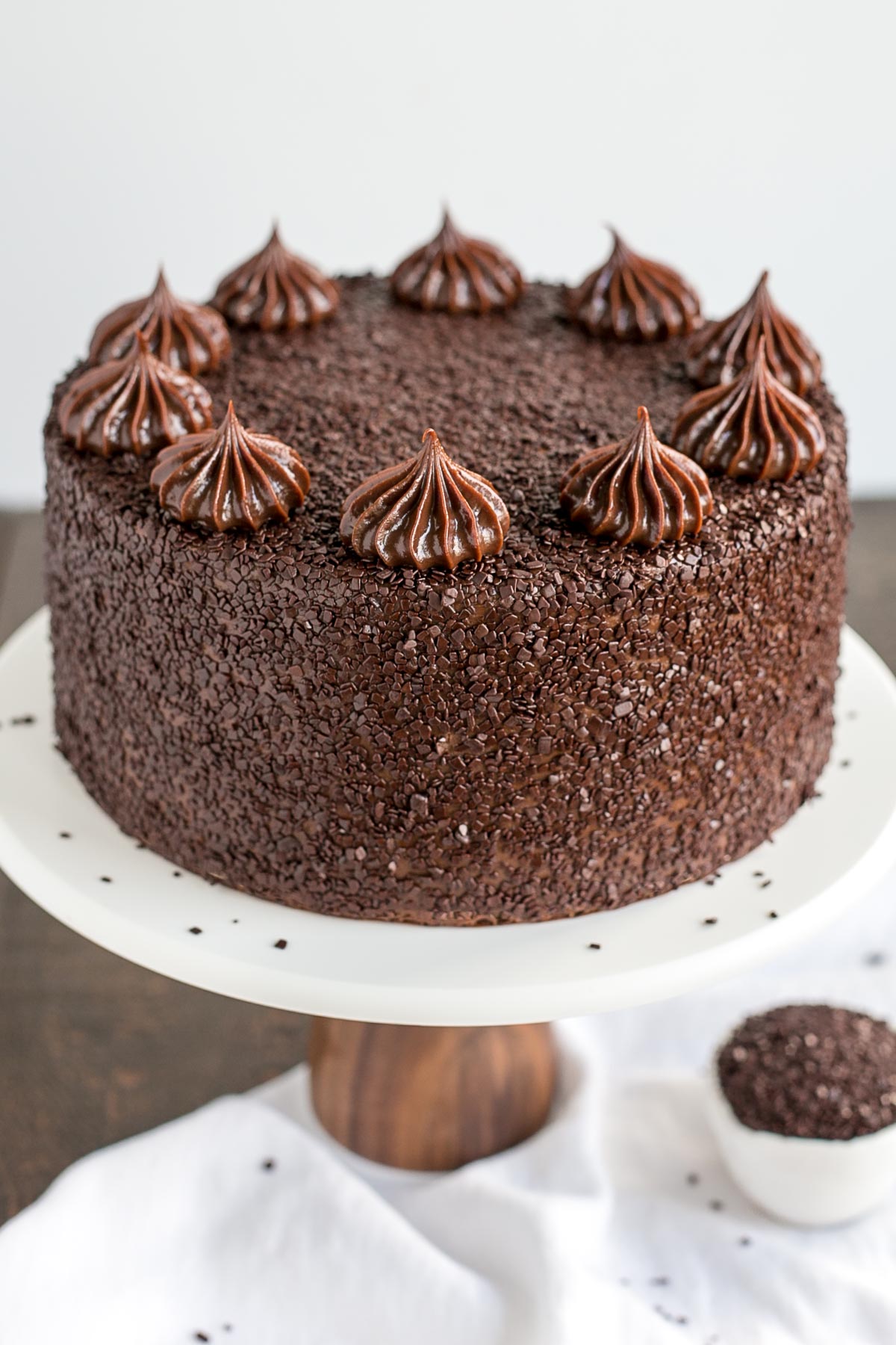 A close up of a chocolate cake on a white cake stand.