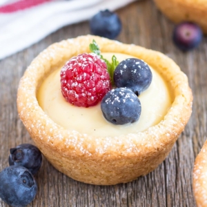 A close up of a cookie cup with fruit on top of a wooden table.