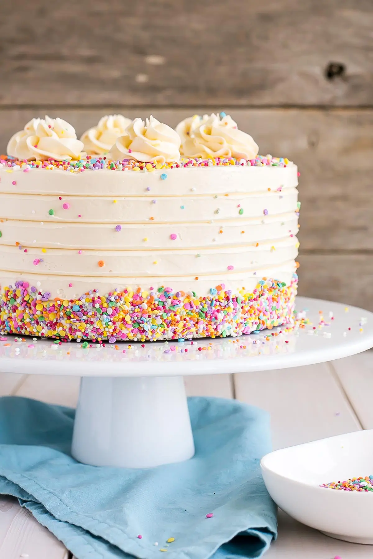 Cake on a white cake stand, decorated with confetti sprinkles.