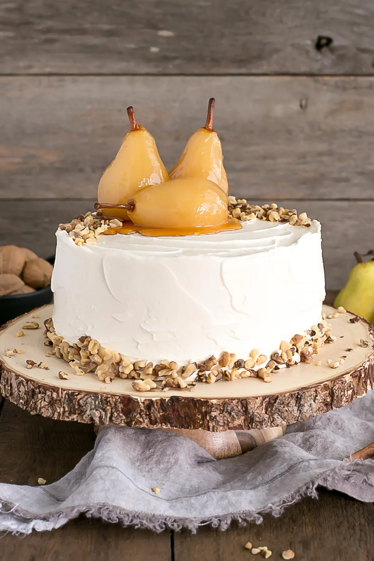 Walnut cake with poached pears on top on a rustic wooden cake stand.