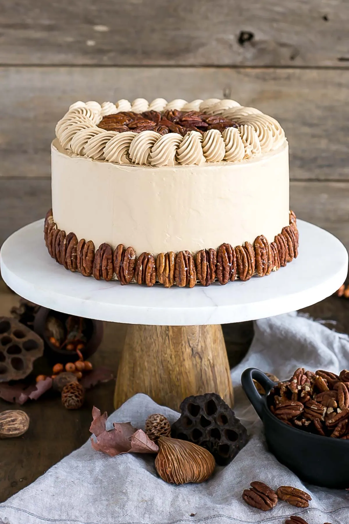 Cake decorated with pecans on a rustic cake stand.
