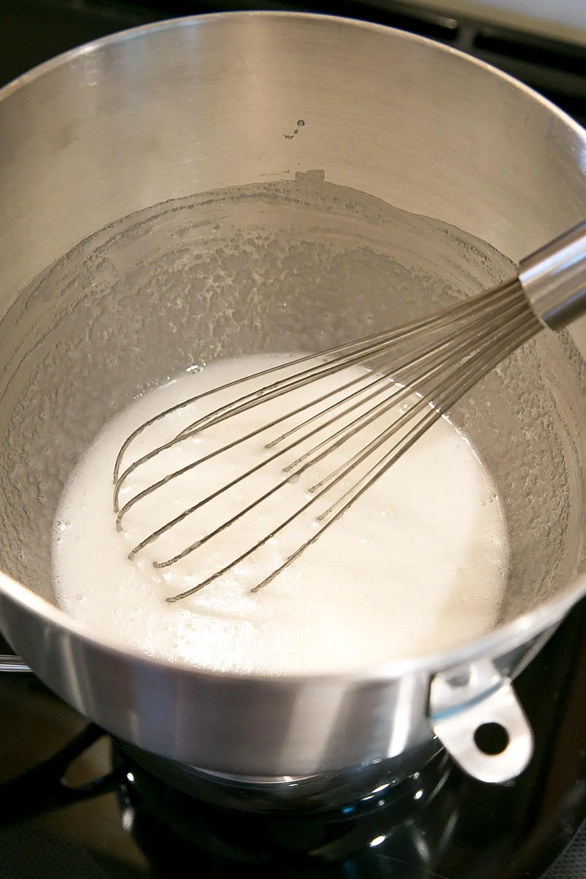 Whisking egg whites and sugar in a bowl over a simmering pot of water.
