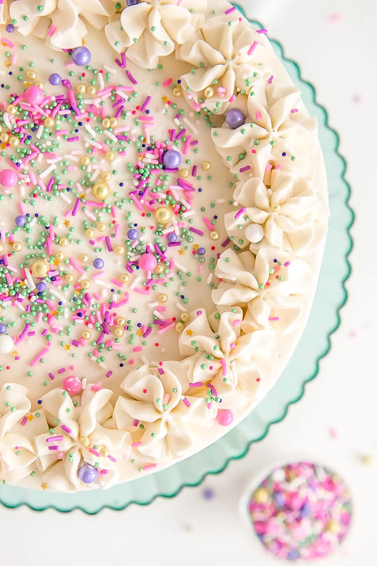 Top down image of a white cake with white buttercream, rosette dollops, and sprinkles.