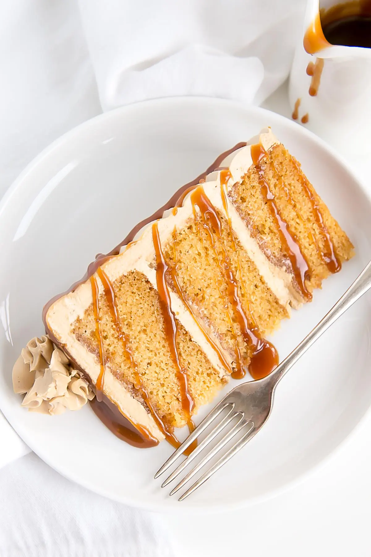 Slice of caramel cake on a plate, drizzled with more caramel.