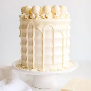 This White Chocolate Cake is both decadent and delicious! White chocolate is incorporated into the cake layers, the frosting, and the drip for a stunning monochrome effect.