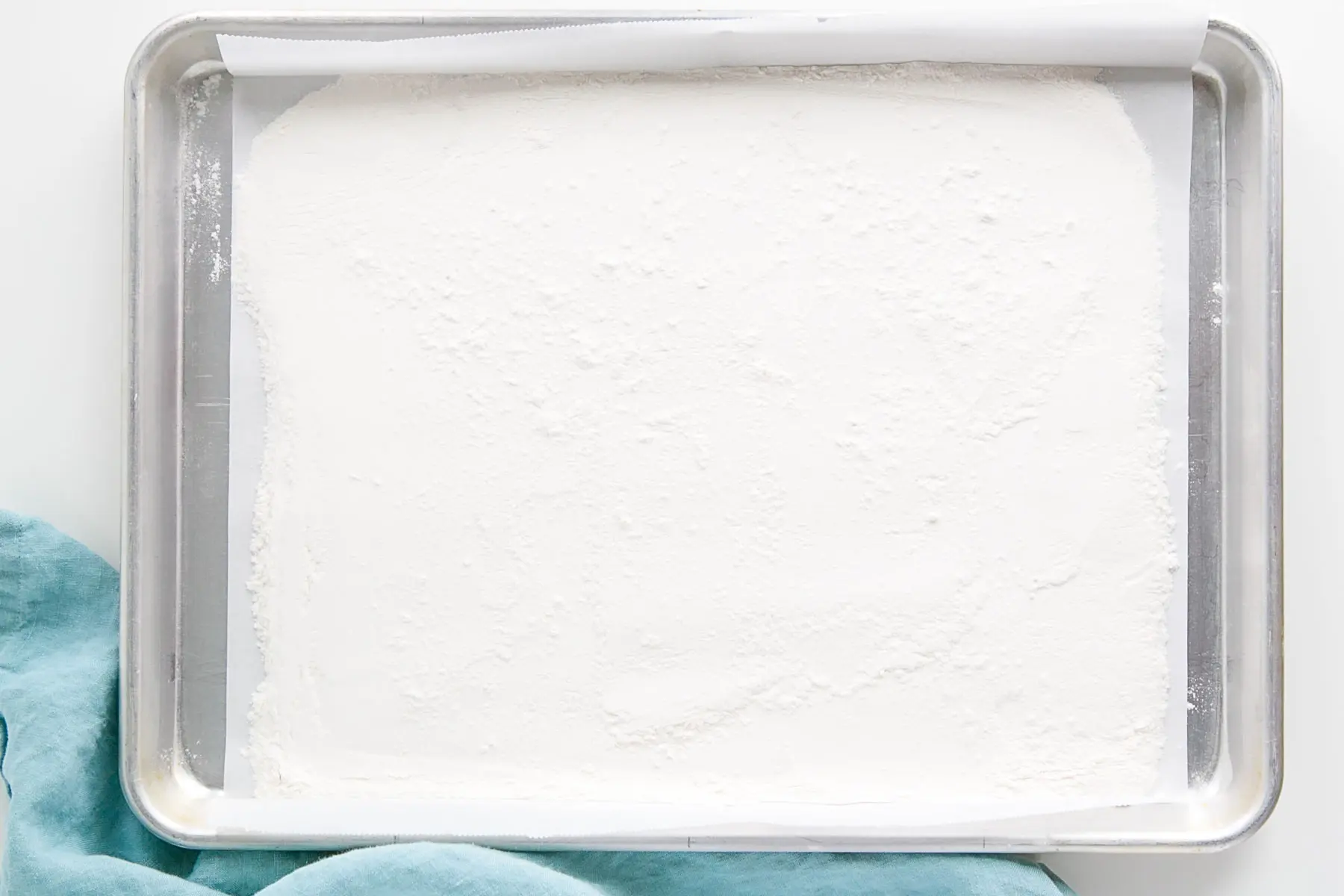 Uncooked flour spread out on a baking sheet lined with parchment.