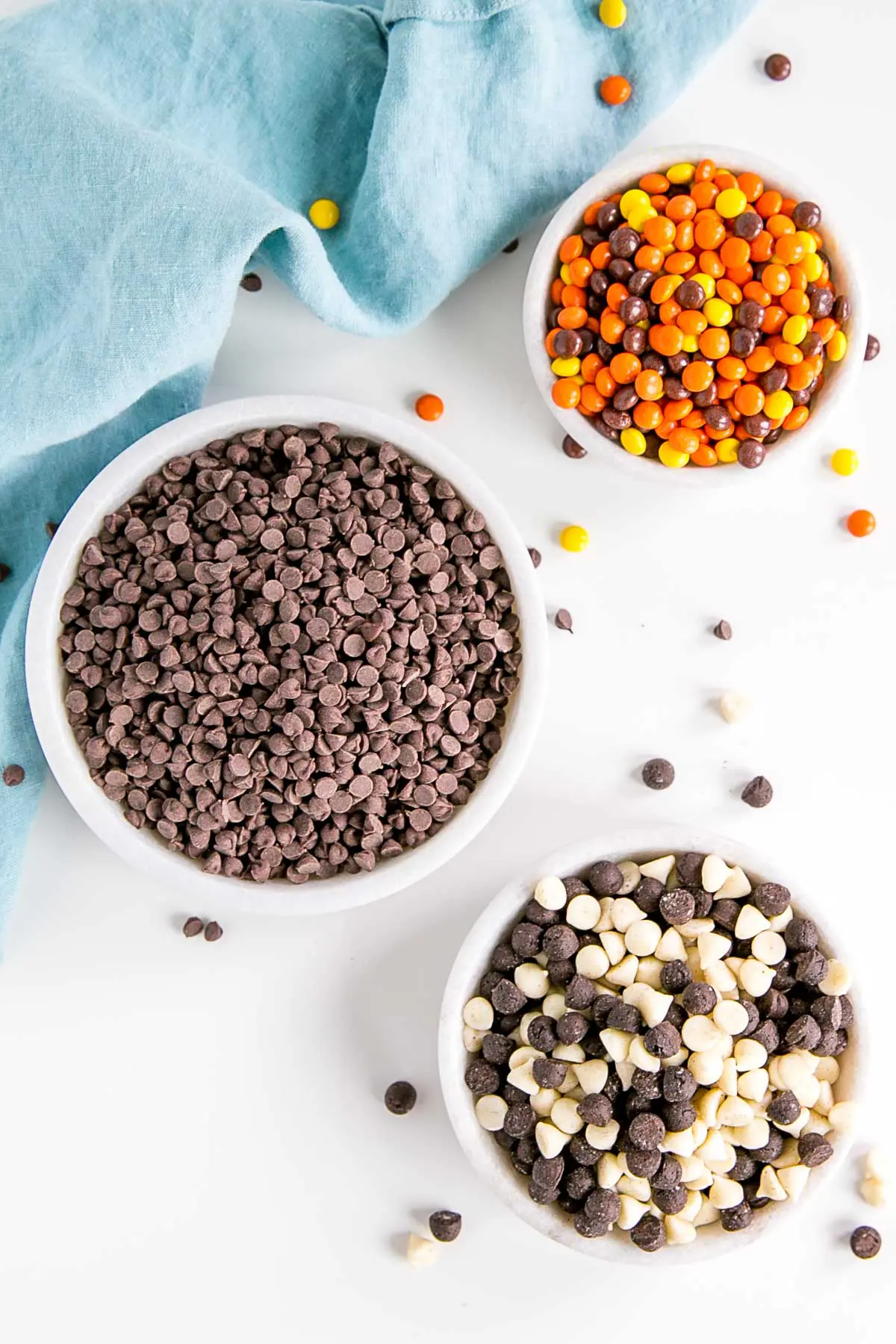 Three bowls filled with chocolate chips, Reese's Pieces, and cookies n' creme chips.