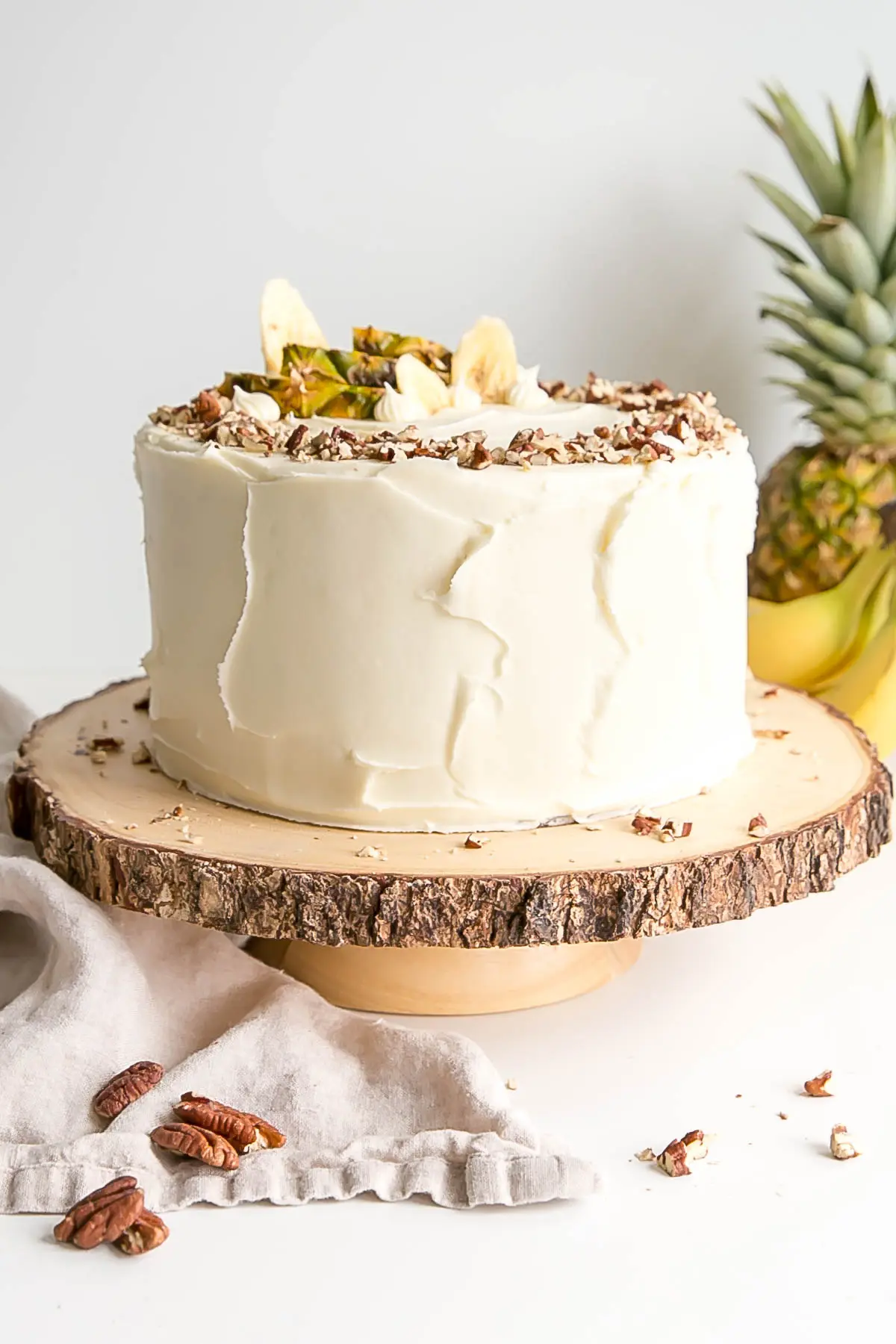 Bolo de beija-flor numa banca de madeira rústica com um ananás e bananas ao fundo.