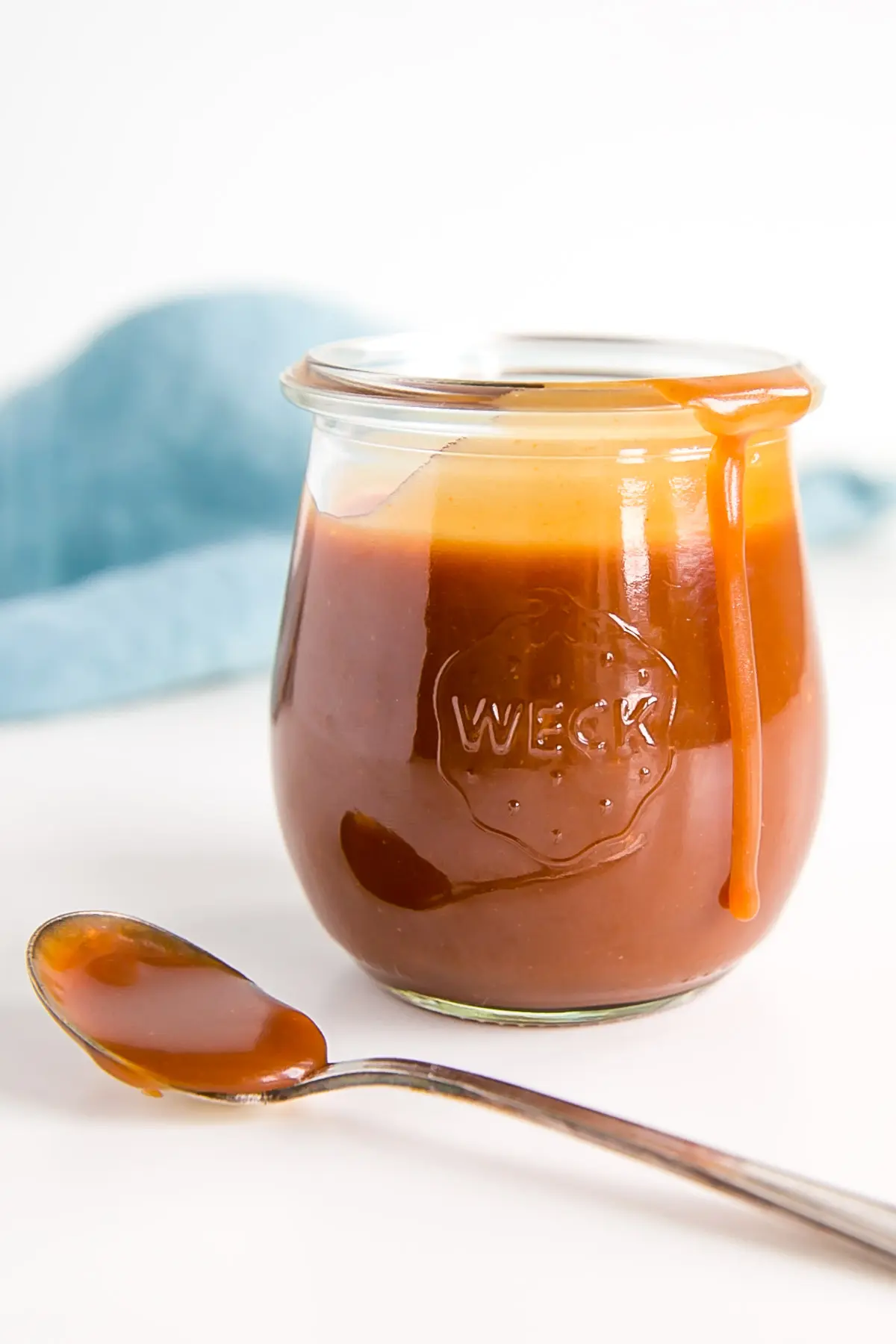 Caramel in a jar with a spoon of caramel beside and a blue cloth in the background