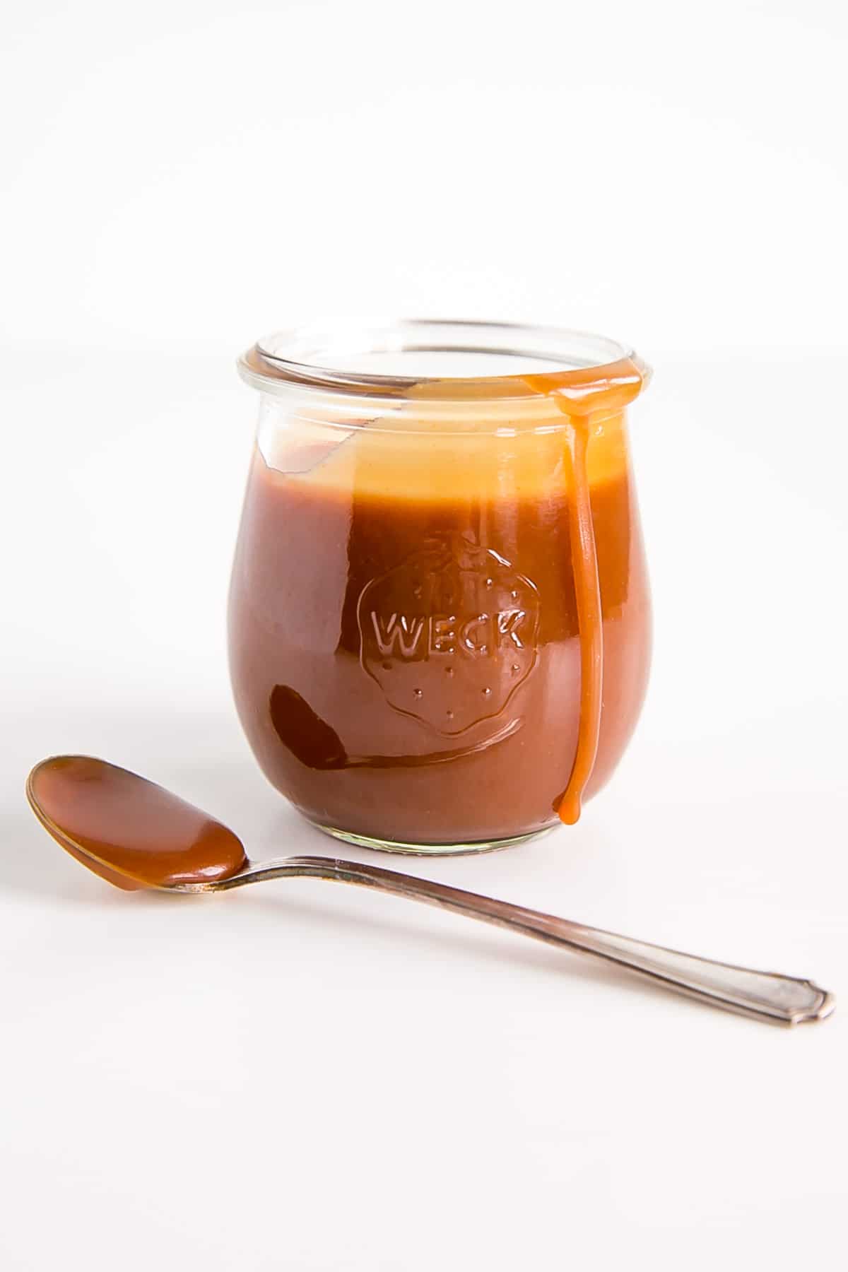 Caramel sauce in a jar with a spoon next to it.