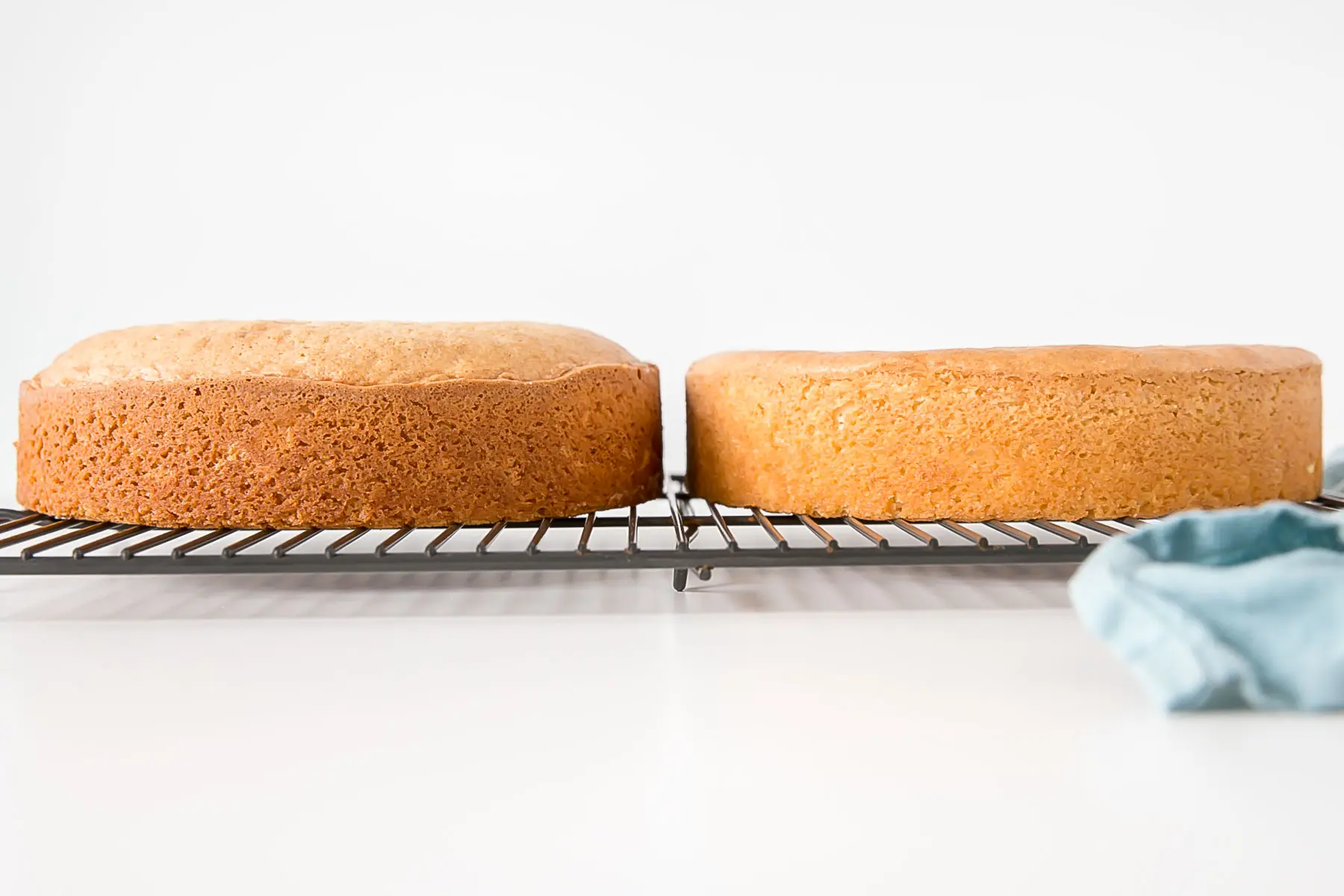 Side-by-side shot of baked cakes on a cooling rack, one that is domed.