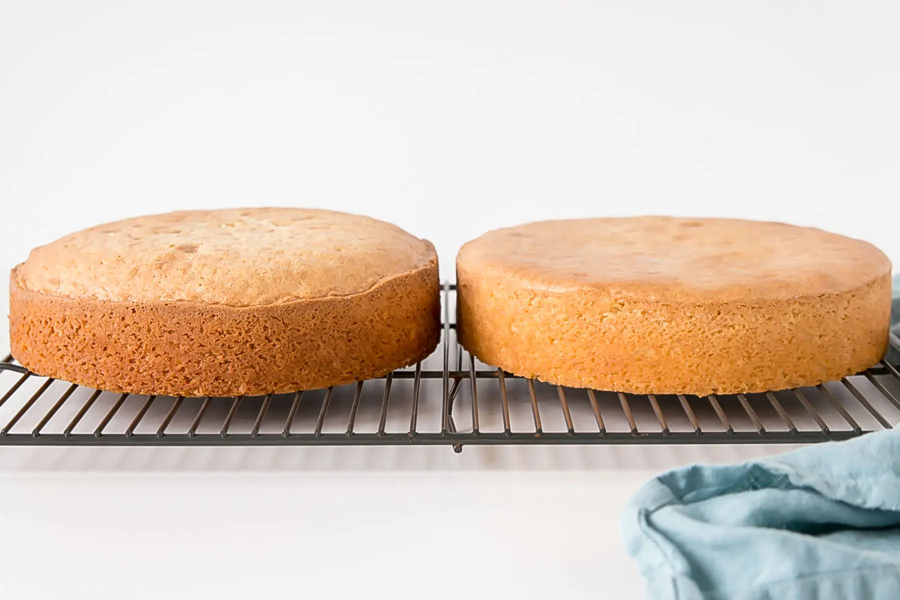 Side-by-side shot of baked cakes on a cooling rack, one that is domed.