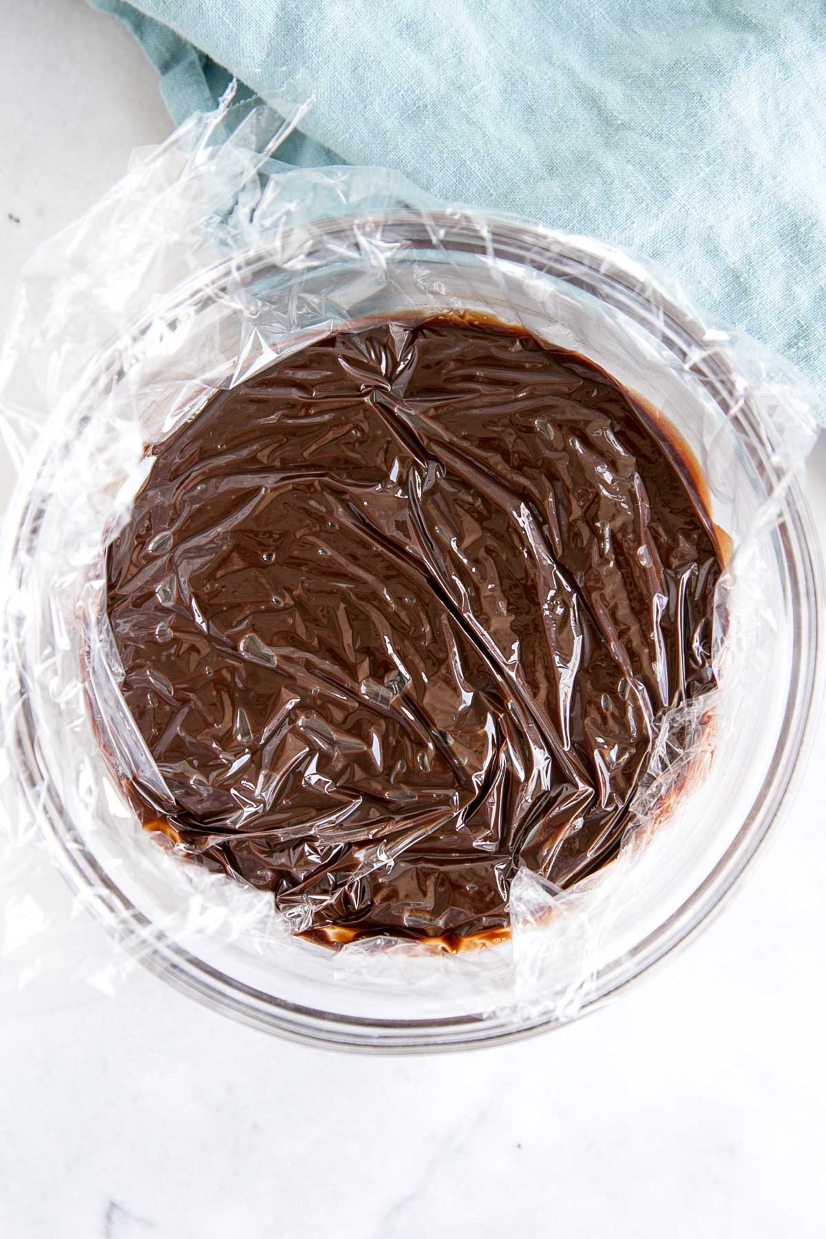Ganache in a bowl with plastic wrap directly on top.