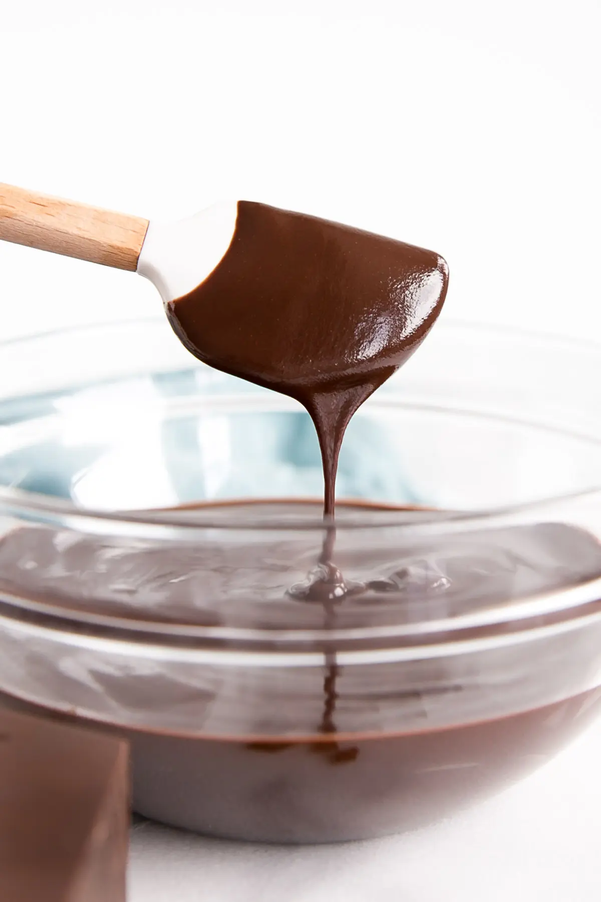 Dark chocolate ganache drizzling off a white spatula into a bowl.