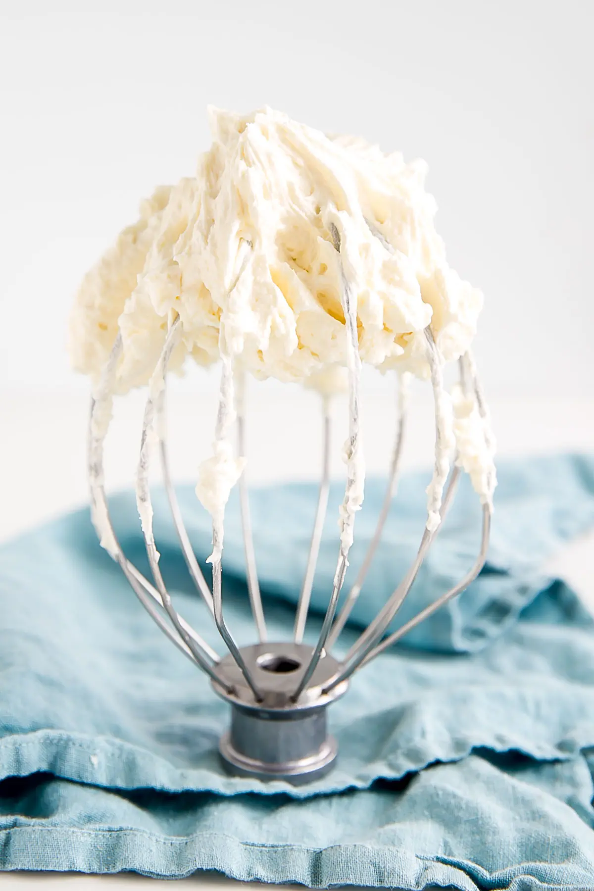 Ermine Frosting on a stand mixer whisk with a blue cloth in the background.