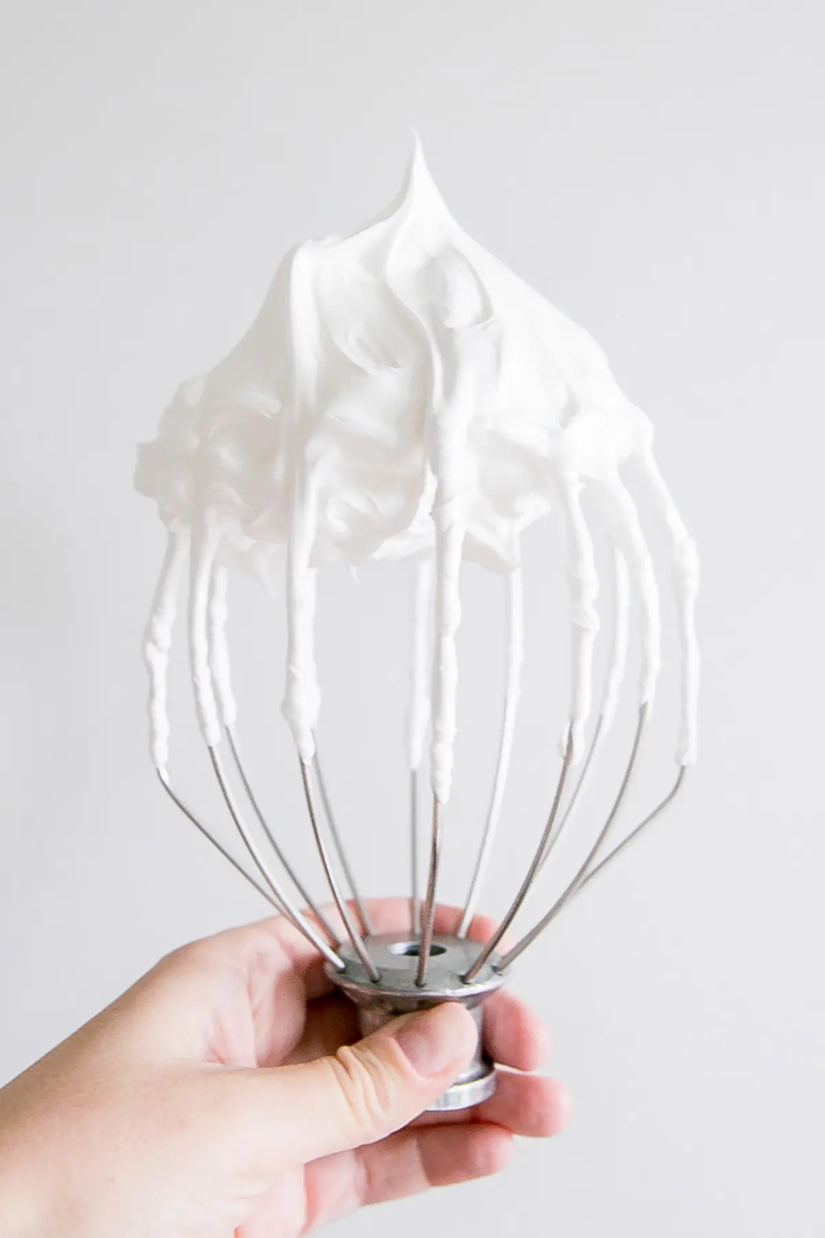 Holding a stand mixer whisk showing a stiff peak meringue.