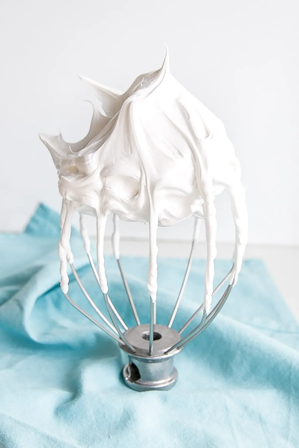 Seven minute frosting on a stand mixer whisk on a blue cloth.