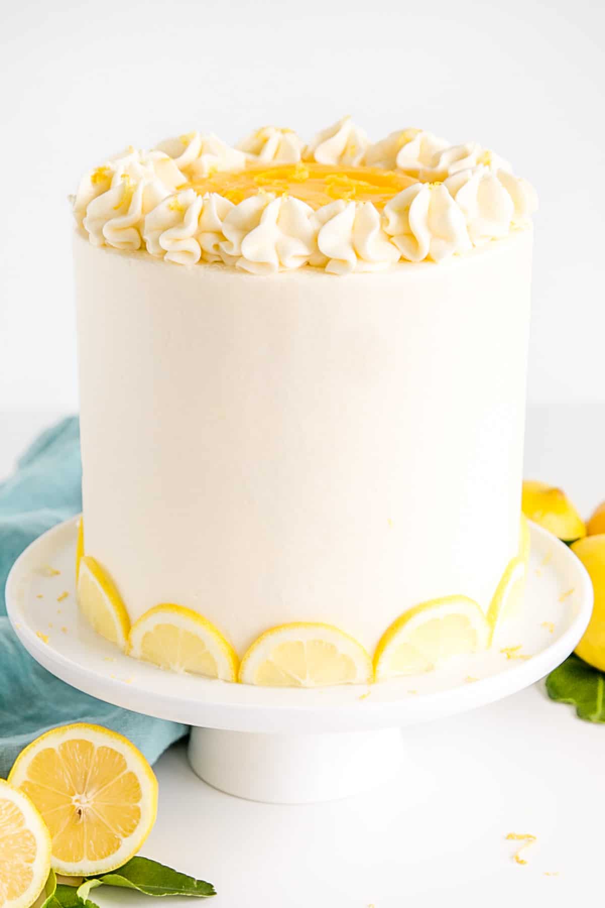 Cake on a white cake stand with lemons in the foreground.