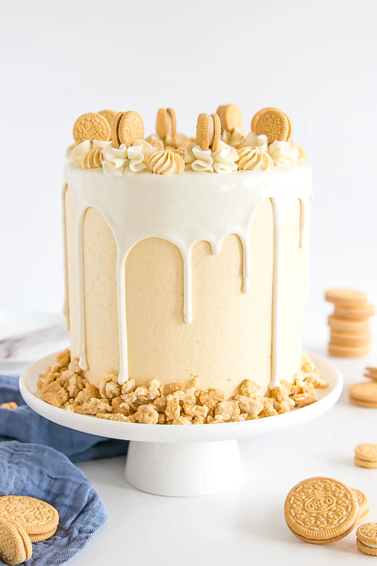 Golden Oreo cake on a white cake stand. Decorated with a white chocolate ganache drip and rosettes on top.